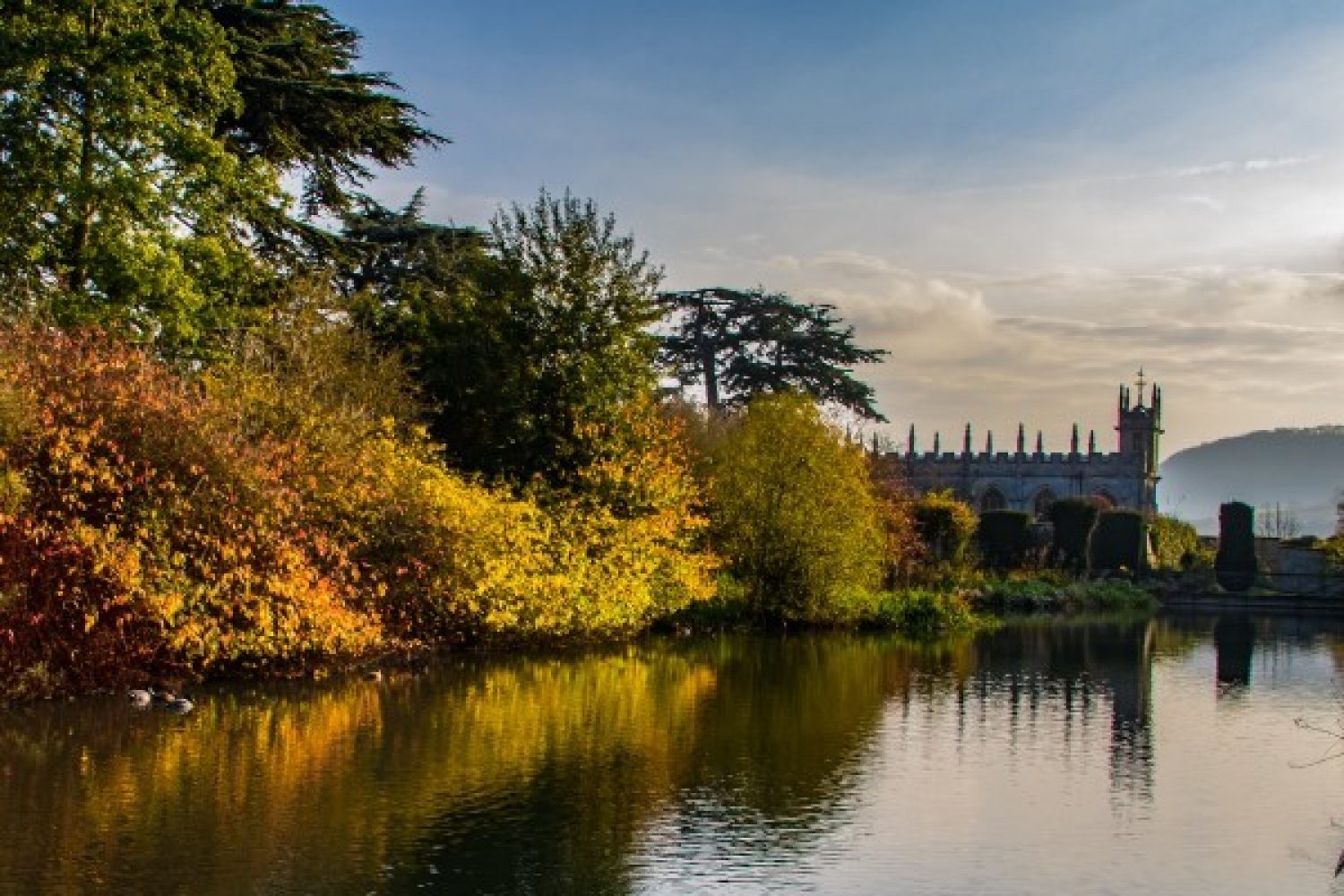 Lakeside photo of autumn coloured foliage at Sudeley