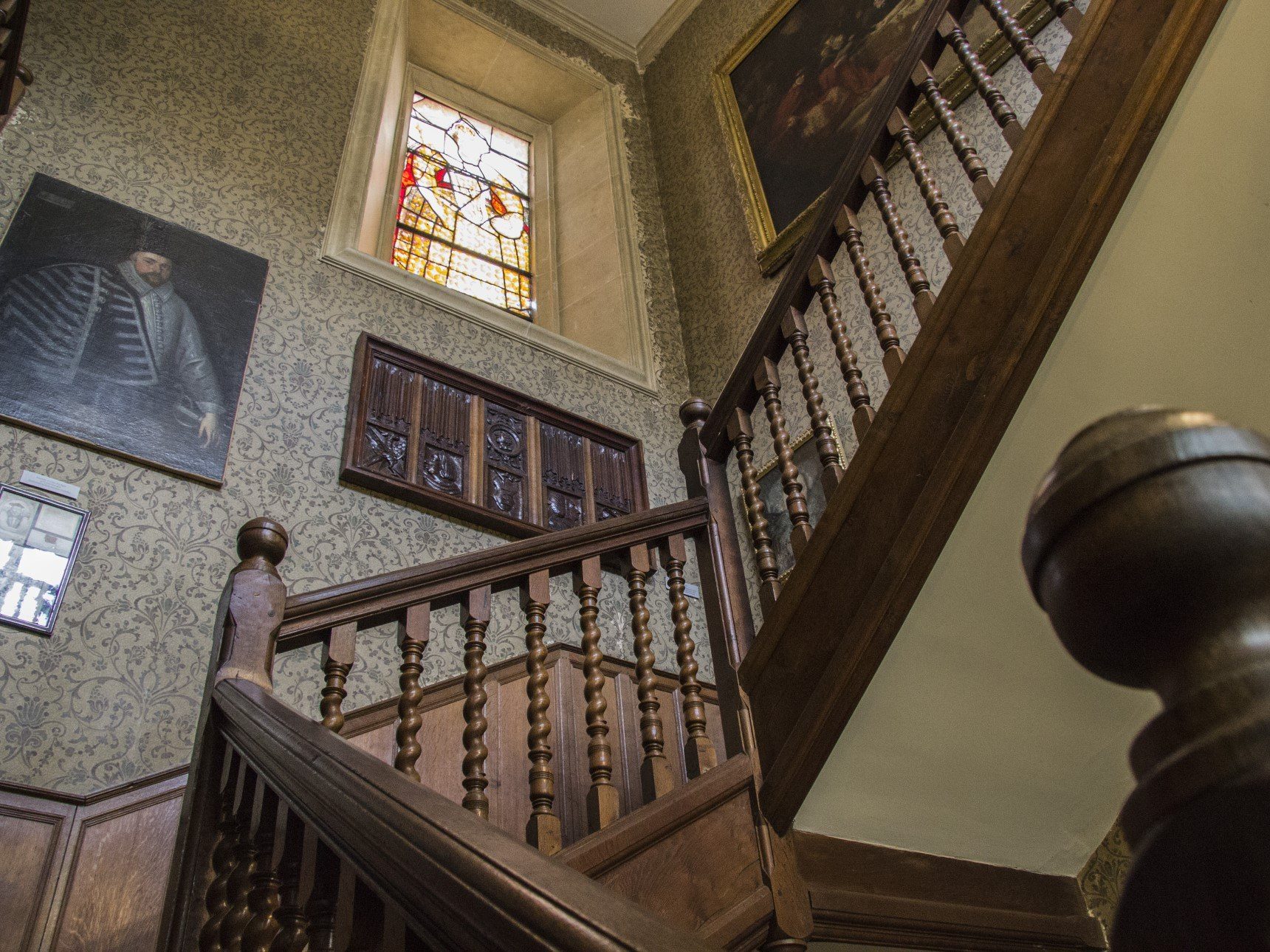 View looking upstairs in South Hall showing a number of paintings on the wall and a stained glass window of Elizabeth I